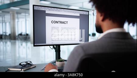 Young man reviewing insurance contract paperwork on desktop computer at office. Stock Photo