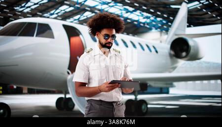 Cheerful African-American pilot using tablet for preflight maintenance checklist. Stock Photo