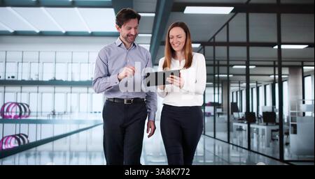 Happy workplace conversation with tablet: two colleagues walk and talk. Stock Photo