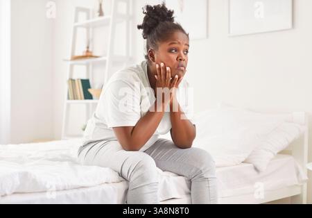 African american woman sitting on comfortable soft bed, feeling worry, lonely, unhappy girl  Stock Photo