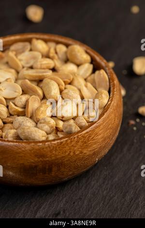fried peanut kernels in a wooden bowl, fried yellow peanuts with a little salt on the table, close up Stock Photo
