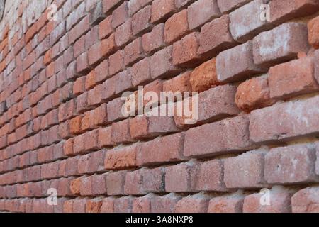 unmaintained old brick wall made of orange old broken bricks with completely chipped plaster Stock Photo