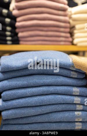 Stack of folded blue wool sweaters with size labels on a wooden shelf in a retail store, showcasing soft fabric and an organized clothing display. Stock Photo