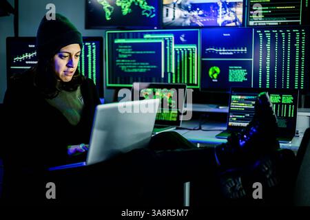 Female hacker breaking into corporate network using laptop and multiple screens Stock Photo