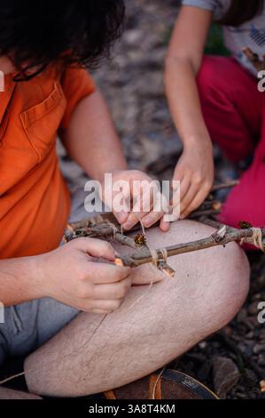 Close-up of a father and daughter tying sticks together with string, creating a handmade woodcraft project outdoors using natural materials. Stock Photo