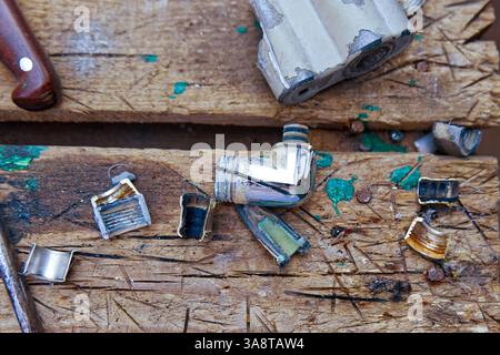A close-up of a well-used wooden workbench, splattered with paint, showcasing various small metal tube wringers. Stock Photo