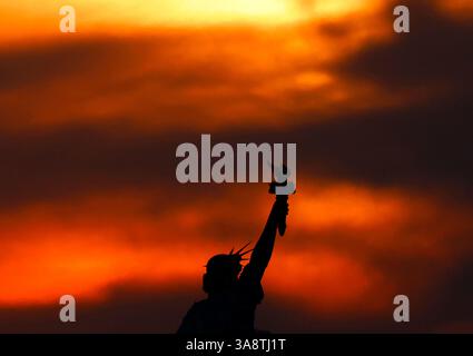Port Liberte, United States. 29th Mar, 2025. The sky shows colors of red and orange as the sun is blocked by clouds behind the Statue of Liberty after sunrise in New Jersey on Saturday, March 29, 2025. Parts of the Northeast were blocked by clouds from seeing a partial solar eclipse Saturday morning, Photo by John Angelillo/UPI Credit: UPI/Ģ����ý Live News Stock Photo