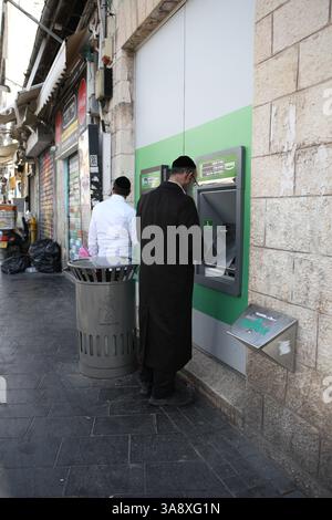 ATM, Jewish men, one Ultra Orthodox, the other Orthodox withdraw money from an automated teller machine to buy with in the market  Yehuda Market. Stock Photo