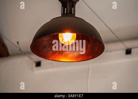 A vintage-style pendant light fixture hangs from the ceiling, casting a warm, inviting glow. The light is on, illuminating the space below Stock Photo