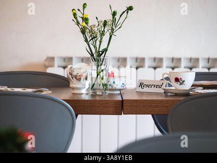 A reserved table is set for afternoon tea, complete with floral china, a sugar bowl, creamer, and a vase of fresh flowers Stock Photo
