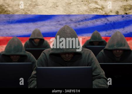 The troll factory. A hacker is sitting at a laptop and against the background of the Russian flag, attacking and hacking corporate servers with a viru Stock Photo