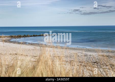 A beach with a rocky shoreline and a calm Baltic sea. The sky is clear and blue, and the water is a deep blue color. The beach is mostly empty, with o Stock Photo