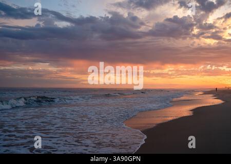 Fiery sunset colors reflect on the wet sand and rolling waves. Stock Photo
