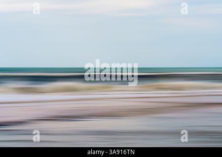 Blurred waves roll gently beneath a soft blue sky. Stock Photo