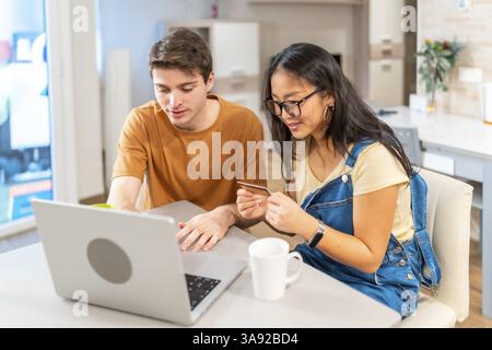 Multiethnic couple using a laptop and a credit card, making online purchases together in their modern apartment Stock Photo