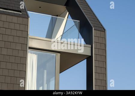Modern architectural detail featuring a glass balcony, dark tile cladding, and a clear blue sky Stock Photo