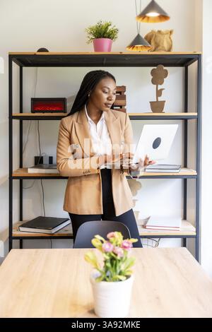 Businesswoman standing in an elegant hotel room, using a laptop to manage her business efficiently while traveling for work Stock Photo