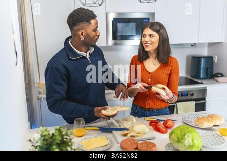 Young multiethnic couple having fun while preparing burgers together in their modern kitchen Stock Photo