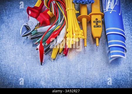 Yellow electrical tester crocodile plugs cable ties blue construction plans nippers on metallic background electricity concept Stock Photo