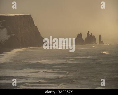 Golden hour view from Dyrhólaey, Iceland, showing the Reynisdrangar sea stacks rising from the ocean mist. Iconic coastal landscape in dramatic winter Stock Photo