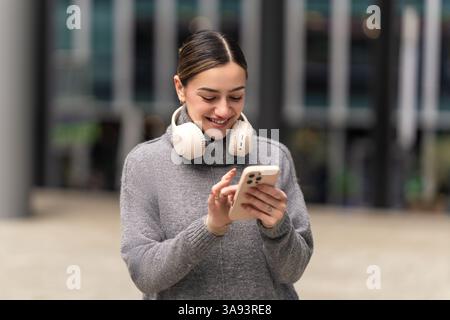 Lost in the lecture, found in the feed. A young student with headphones and smartphone multitasks between online learning and social media, blending Stock Photo