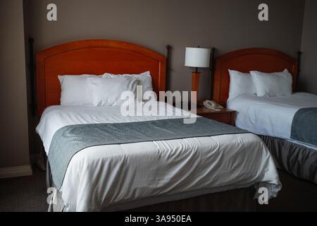 Two beds in a casino hotel room with a wooden headboard, white sheets and pillows with grey blanket. Lamp and telephone on the night table. Stock Photo