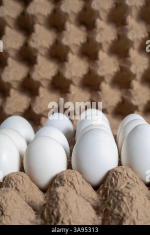 A close-up view of white eggs placed in a paper carton tray against a textured background. Stock Photo