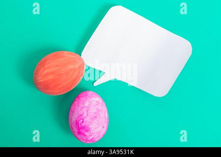 Brightly colored Easter eggs with a blank paper speech bubble on a teal background, perfect for seasonal designs. Stock Photo