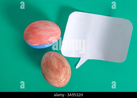 A colorful painted egg and paper speech bubble placed on a vibrant green surface, communication, and festive decorations. Stock Photo