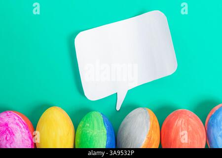 A vibrant display of painted Easter eggs lined up with a plain white speech bubble on a bright blue background. Perfect for creative communication, Ea Stock Photo