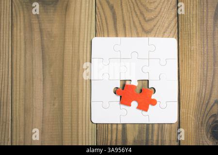 A puzzle piece is missing from a puzzle, and a red piece is sitting on top of the empty space. Concept of completion and satisfaction, as the puzzle i Stock Photo