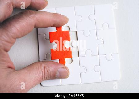 A person is holding a puzzle piece with a red dot on it. The puzzle piece is missing, and the person is trying to find it. Concept of determination an Stock Photo