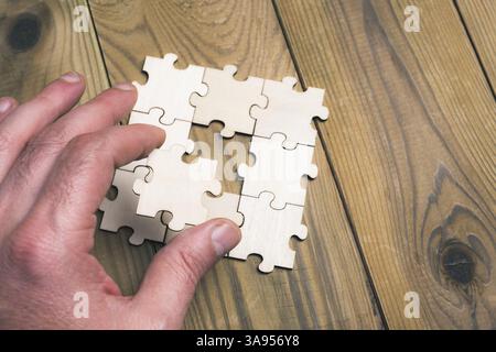 A hand is holding a puzzle piece that is missing. The puzzle piece is part of a larger puzzle, and the missing piece is the key to completing it Stock Photo