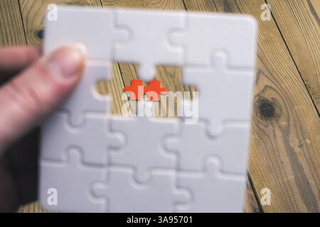 A person is holding a puzzle piece with a red piece missing. Concept of missing something important or incomplete Stock Photo
