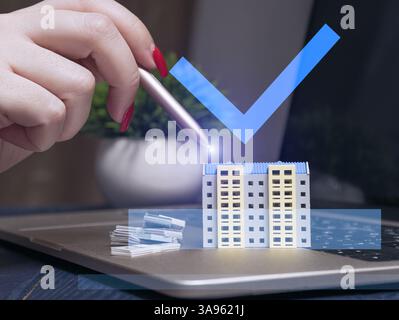 A hand using a stylus interacts with a virtual model of an apartment building on a laptop, symbolizing digital real estate investment. Stock Photo