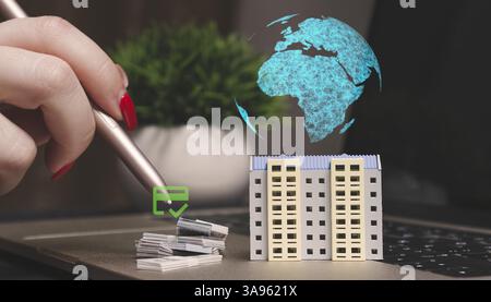 A hand using a stylus interacts with a virtual model of an apartment building on a laptop, symbolizing digital real estate investment. Stock Photo