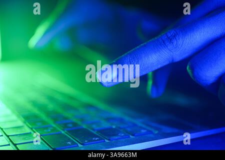 hacker typing on keyboard illuminated by green and blue light Stock Photo