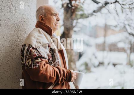 Elderly man enjoying a quiet winter moment outdoors with a warm drink Stock Photo