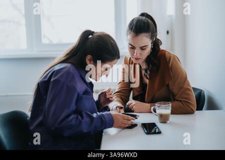 Two young women collaborating with technology over coffee in a modern office setting Stock Photo
