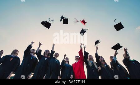 Happy students in academic gowns tossing graduation caps in the air to celebrate their achievement Stock Photo