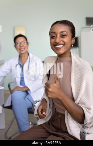 Cheerful young African patient woman recommending clinic, showing thumb up Stock Photo