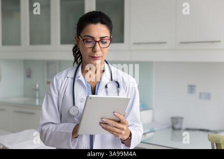 Focused mature physician woman using modern technology on digital tablet Stock Photo
