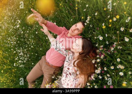 Couple of young people lying down on grass in field of flowers .  Stock Photo