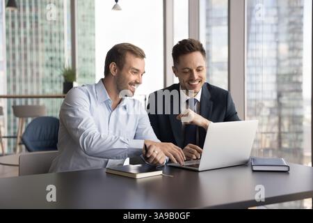 Two laughing multiethnic teammates cooperating on on-line project Stock Photo