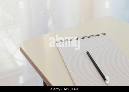 A black pencil on opened  notepad  on white table , place of work  or educational subject Stock Photo
