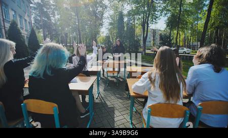 High school students raising hands to answer teacher's question during open air lesson in schoolyard Stock Photo