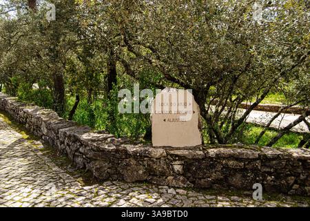 Fatima, Portugal - March 24, 2025: Marked stone along a rustic pathway surrounded by trees in Fatima's greenery Stock Photo