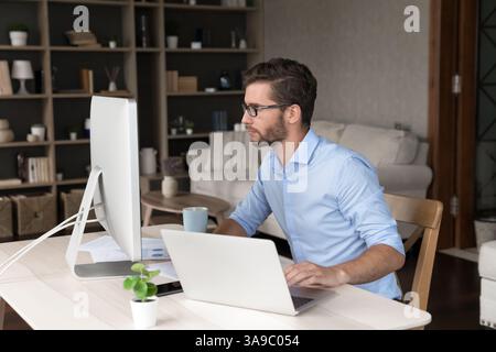 Young man freelancer using laptop and desktop computers at work Stock Photo