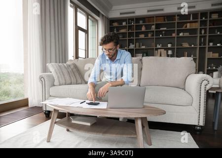 Busy gen z man review financial papers using notebook calculator Stock Photo