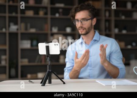 Confident young man speak to smartphone fixed on tripod Stock Photo